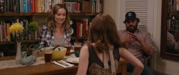 Movie still from “Drinking Buddies” (2013), directed by Joe Swanberg – A woman sitting at a table in front of two other people; Medium shot, Over the shoulder angle