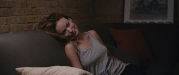 Movie still from “Drinking Buddies” (2013), directed by Joe Swanberg – A beautiful young lady sitting on top of a couch; Medium shot, Over the shoulder angle
