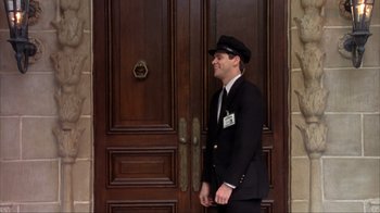 Movie still from “Dumb and Dumber” (1994), directed by Peter Farrelly – A doorman standing in front of a wooden door; Wide shot, Low angle