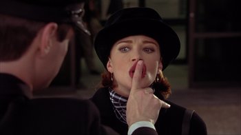 Movie still from “Dumb and Dumber” (1994), directed by Peter Farrelly – A woman in a black hat is holding her finger to her lips; Close Up shot, Over the shoulder angle