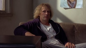 Movie still from “Dumb and Dumber” (1994), directed by Peter Farrelly – A man sitting on top of a couch in a living room; Medium shot, Low angle
