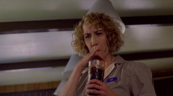 Movie still from “Dumb and Dumber” (1994), directed by Peter Farrelly – A woman with curly hair is drinking from a glass; Close Up shot, Low angle