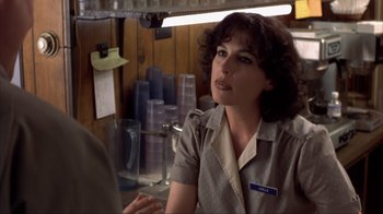 Movie still from “Dumb and Dumber” (1994), directed by Peter Farrelly – A woman sitting at a table in front of a stack of cups; Close Up shot, Over the shoulder angle