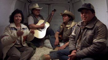 Movie still from “Dumb and Dumber” (1994), directed by Peter Farrelly – A group of men sitting on the ground with a guitar; Wide shot, High angle