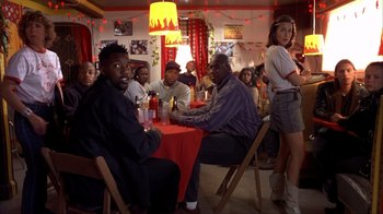 Movie still from “Dumb and Dumber” (1994), directed by Peter Farrelly – A group of men and women sitting at a table; Medium shot, Low angle
