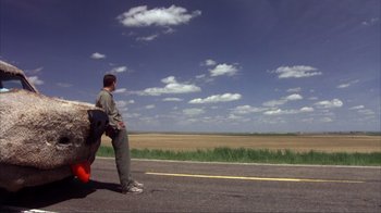 Movie still from “Dumb and Dumber” (1994), directed by Peter Farrelly – A man sitting on the side of a road; Extreme Wide shot, Low angle