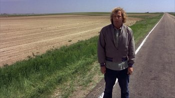 Movie still from “Dumb and Dumber” (1994), directed by Peter Farrelly – A man standing on the side of a road near a field; Wide shot, Over the shoulder angle