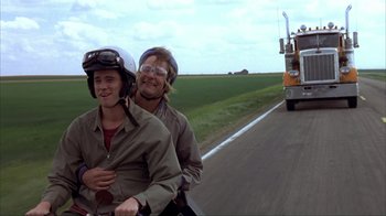 Movie still from “Dumb and Dumber” (1994), directed by Peter Farrelly – Two people riding a motorcycle down a road; Wide shot, Low angle