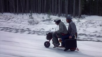 Movie still from “Dumb and Dumber” (1994), directed by Peter Farrelly – Two people riding a small bike in the snow; Wide shot, High angle