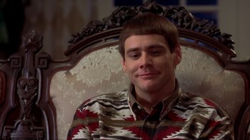 Movie still from “Dumb and Dumber” (1994), directed by Peter Farrelly – A young man sitting in a chair wearing a colorful shirt; Close Up shot, High angle