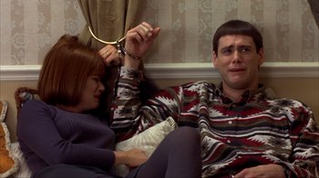 Movie still from “Dumb and Dumber” (1994), directed by Peter Farrelly – A man and a woman sitting on a couch holding handcuffs; Medium shot, High angle