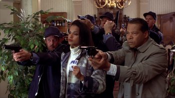 Movie still from “Dumb and Dumber” (1994), directed by Peter Farrelly – A group of people holding guns in a room; Medium shot, Low angle