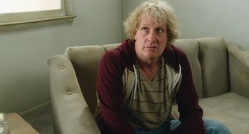Movie still from “Dumb and Dumber To” (2014), directed by Peter Farrelly – A man sitting on a couch looking at the camera; Medium shot, Over the shoulder angle