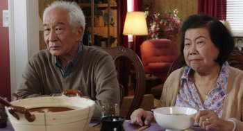Movie still from “Dumb and Dumber To” (2014), directed by Peter Farrelly – An older man and woman sitting at a dinner table with bowls of food; Medium shot, Over the shoulder angle
