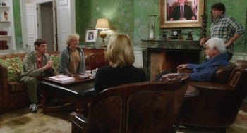 Movie still from “Dumb and Dumber To” (2014), directed by Peter Farrelly – A group of people sitting at a table in front of a fireplace; Wide shot, Over the shoulder angle