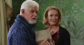 Movie still from “Dumb and Dumber To” (2014), directed by Peter Farrelly – An older man holding a gift box next to a woman; Medium shot, Over the shoulder angle