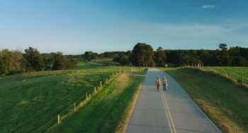 Movie still from “Dumb and Dumber To” (2014), directed by Peter Farrelly – A group of people walking down a road near a field; Extreme Wide shot, High angle