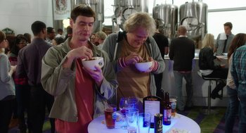 Movie still from “Dumb and Dumber To” (2014), directed by Peter Farrelly – Two men are standing at a table with drinks; Medium shot, High angle