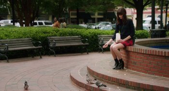 Movie still from “Dumb and Dumber To” (2014), directed by Peter Farrelly – A woman sitting on a brick wall near a bird; Wide shot, High angle