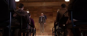 Movie still from “Dying of the Light” (2014), directed by Paul Schrader – A man in a suit standing in front of a group of people; Wide shot, Low angle