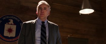 Movie still from “Dying of the Light” (2014), directed by Paul Schrader – A man in a suit and tie standing in front of a wooden wall; Close Up shot, Low angle