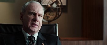 Movie still from “Dying of the Light” (2014), directed by Paul Schrader – An older man wearing a suit and tie in front of a fan; Close Up shot, Over the shoulder angle