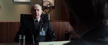 Movie still from “Dying of the Light” (2014), directed by Paul Schrader – An older man sitting at a desk in a suit; Medium shot, Over the shoulder angle