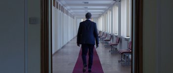 Movie still from “Dying of the Light” (2014), directed by Paul Schrader – A man in a suit is walking down a hallway; Wide shot, Over the shoulder angle