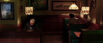 Movie still from “Dying of the Light” (2014), directed by Paul Schrader – Two people sitting at a booth in a restaurant; Wide shot, High angle