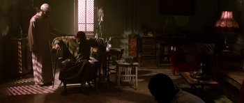 Movie still from “Dying of the Light” (2014), directed by Paul Schrader – A man sitting on a chair reading a book; Wide shot, High angle