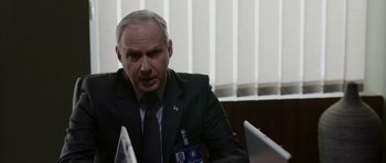 Movie still from “Dying of the Light” (2014), directed by Paul Schrader – An older man wearing a suit and tie sitting in front of a computer; Close Up shot, Over the shoulder angle