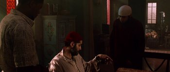 Movie still from “Dying of the Light” (2014), directed by Paul Schrader – A man wearing a red hat is sitting at a table; Medium shot, Over the shoulder angle