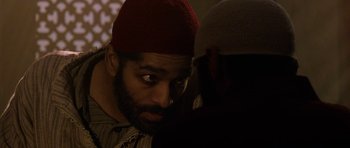 Movie still from “Dying of the Light” (2014), directed by Paul Schrader – A man with a beard and a red hat looking at another man; Close Up shot, Over the shoulder angle