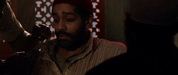 Movie still from “Dying of the Light” (2014), directed by Paul Schrader – A man with a beard wearing a red hat and a striped shirt; Close Up shot, Over the shoulder angle