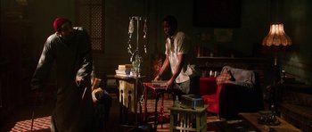 Movie still from “Dying of the Light” (2014), directed by Paul Schrader – A man standing in front of a table in a living room; Wide shot, Over the shoulder angle