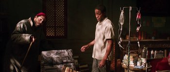 Movie still from “Dying of the Light” (2014), directed by Paul Schrader – A man standing in front of a pile of books; Medium shot, High angle