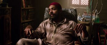 Movie still from “Dying of the Light” (2014), directed by Paul Schrader – A man in a red hat sitting on a couch; Medium shot, High angle