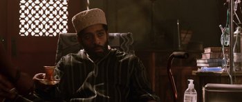 Movie still from “Dying of the Light” (2014), directed by Paul Schrader – A man wearing a hat sitting in a chair; Close Up shot, Low angle