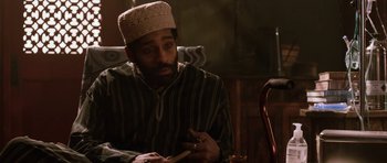 Movie still from “Dying of the Light” (2014), directed by Paul Schrader – A man with a beard wearing a hat and sitting in a chair; Close Up shot, Over the shoulder angle