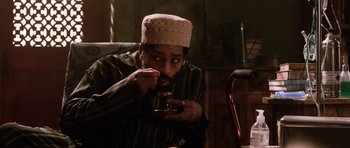 Movie still from “Dying of the Light” (2014), directed by Paul Schrader – A man with a beard and a hat is eating something; Medium shot, High angle