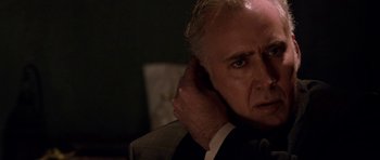 Movie still from “Dying of the Light” (2014), directed by Paul Schrader – An older man is holding his head with one hand and his other hand behind his ear; Close Up shot, Over the shoulder angle