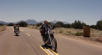 Movie still from “Easy Rider” (1969), directed by Dennis Hopper – A man riding a motorcycle down the middle of the road; Wide shot, Low angle