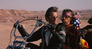 Movie still from “Easy Rider” (1969), directed by Dennis Hopper – A man on a motorcycle next to another man in the desert; Medium shot, Low angle