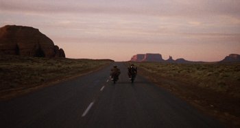 Movie still from “Easy Rider” (1969), directed by Dennis Hopper – Two people riding motorcycles down a road at dusk; Extreme Wide shot, High angle