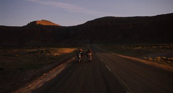 Movie still from “Easy Rider” (1969), directed by Dennis Hopper – A group of people riding motorcycles down the middle of a road; Extreme Wide shot, Low angle