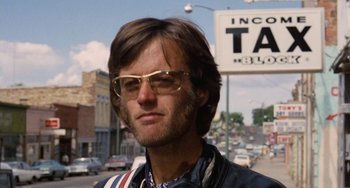 Movie still from “Easy Rider” (1969), directed by Dennis Hopper – A person wearing glasses near a street sign; Close Up shot, Low angle