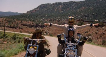 Movie still from “Easy Rider” (1969), directed by Dennis Hopper – A group of people riding motorcycles down a dirt road; Wide shot, Low angle
