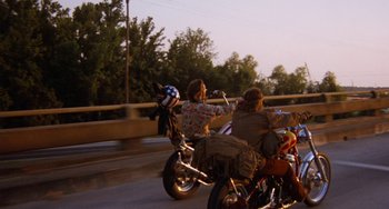 Movie still from “Easy Rider” (1969), directed by Dennis Hopper – Two people riding motorcycles down a street at dusk; Wide shot, Low angle