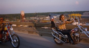 Movie still from “Easy Rider” (1969), directed by Dennis Hopper – A man riding a motorcycle down a street; Wide shot, Low angle