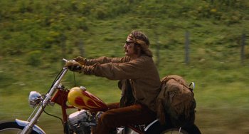 Movie still from “Easy Rider” (1969), directed by Dennis Hopper – A man riding a motorcycle on the side of the road; Wide shot, Low angle